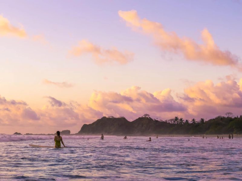 Surfeurs dans les eaux calmes de Playa Guiones au coucher du soleil, Nosara, Costa Rica.