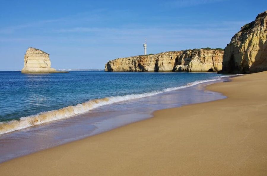 Une plage de sable doré bordée de falaises calcaires, avec des vagues douces et une mer bleu azur sous un ciel dégagé.