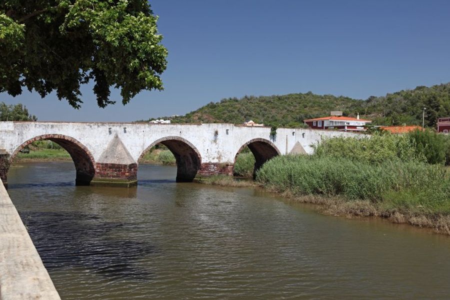 Vue du pont romain traversant la rivière Arade à Silves, entouré de verdure et de collines.