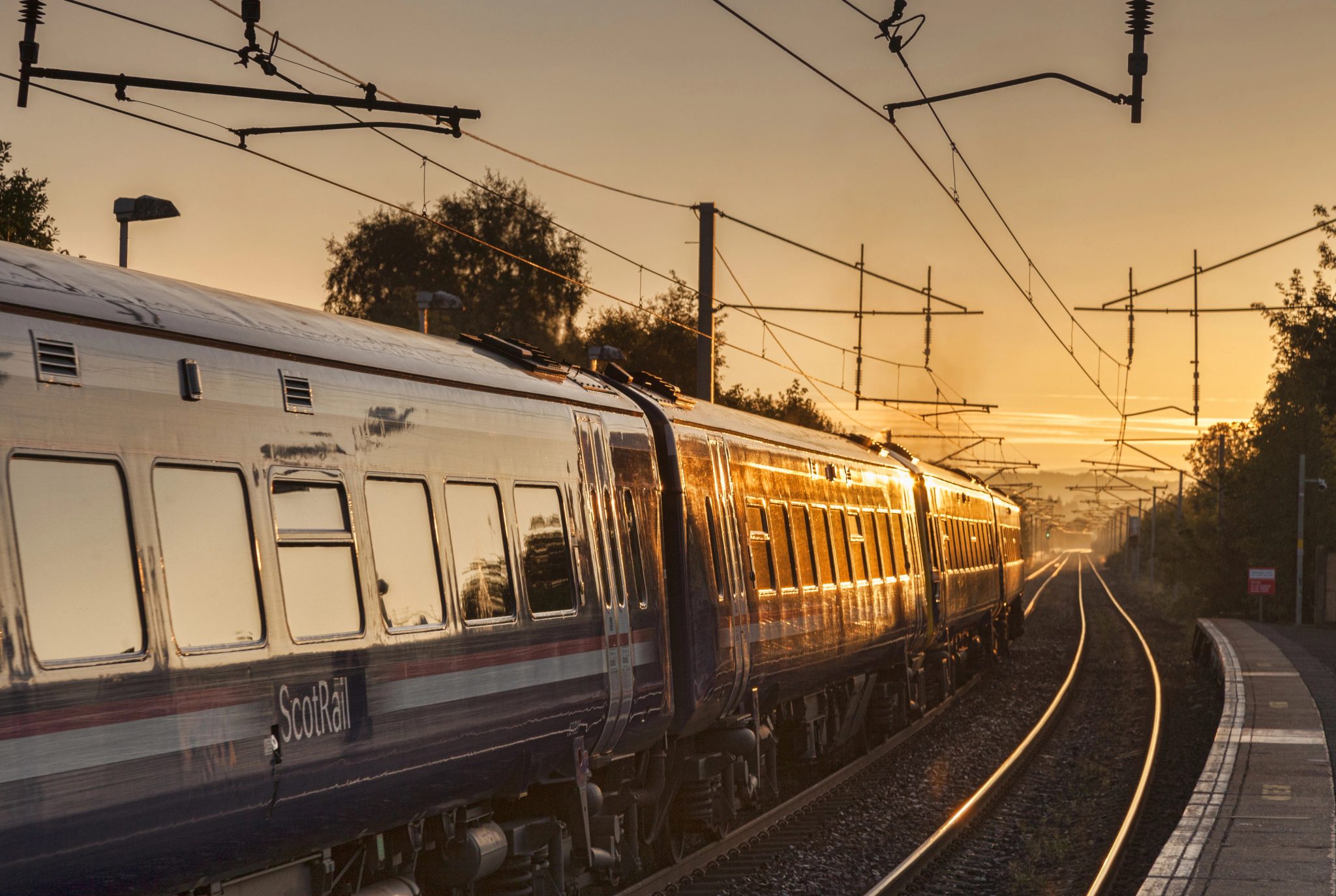 Un train ScotRail à quai sous les caténaires, éclairé par la lumière du soleil couchant