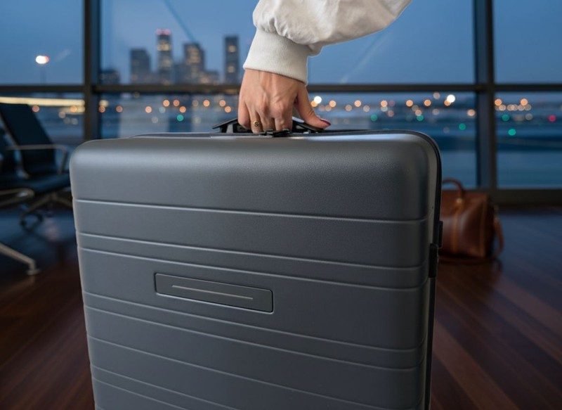 Valise Horizn posée sur un sol en bois dans un salon design avec canapé rouge et lumière tamisée.