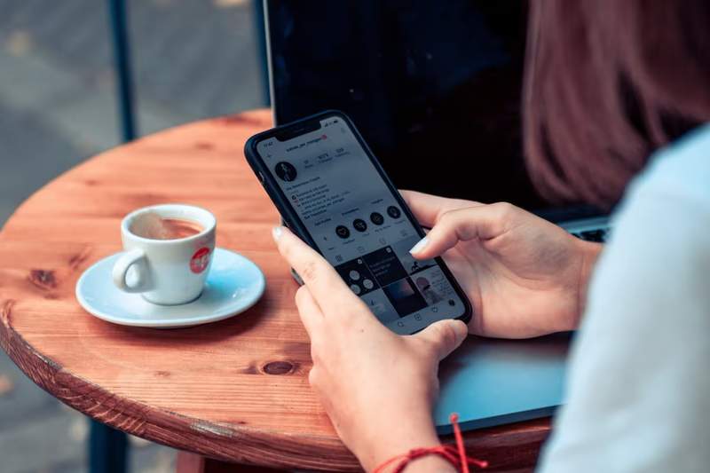 Femme utilisant son smartphone avec une e-SIM en Albanie, assise à la terrasse d’un café avec un café posé sur la table