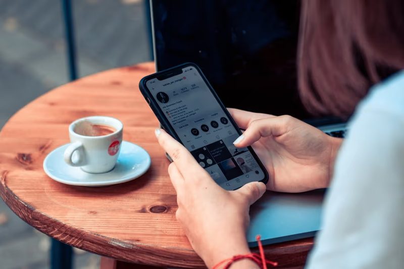 Femme utilisant son smartphone avec une e-SIM en Albanie, assise à la terrasse d’un café avec un café posé sur la table