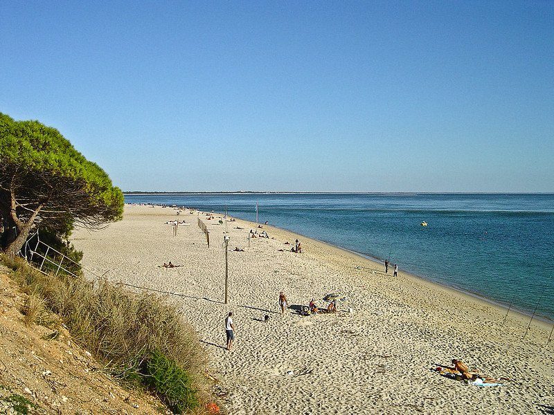 Plage de Figueirinha à Setúbal, Portugal, avec des vacanciers se relaxant sur le sable et une mer calme en arrière-plan.