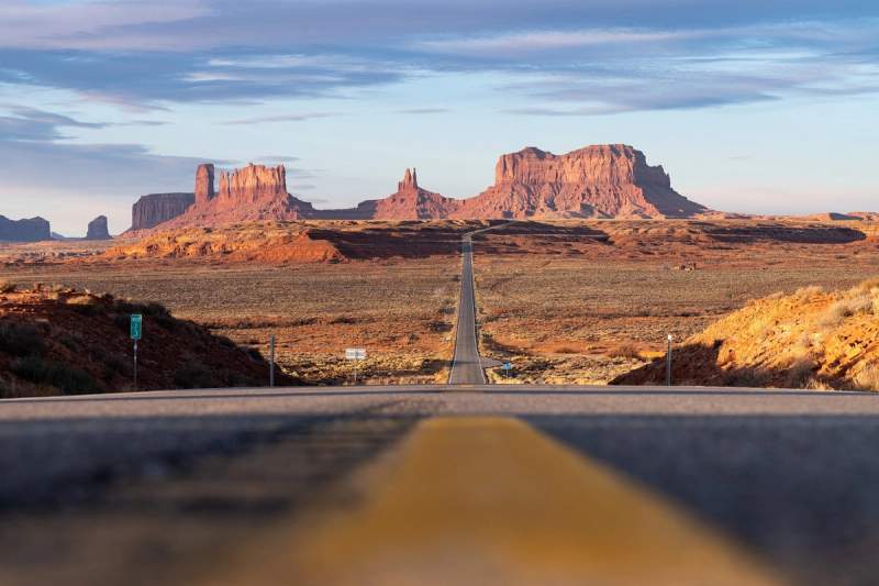 Route menant à Monument Valley, avec ses formations rocheuses emblématiques sous un ciel dégagé, symbolisant l'immensité des paysages américains.