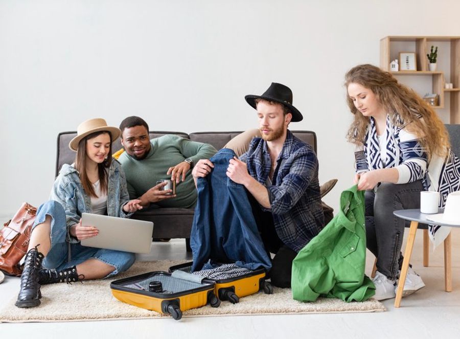 Groupe de quatre amis en train de préparer leurs valises et accessoires de voyage pour un road trip