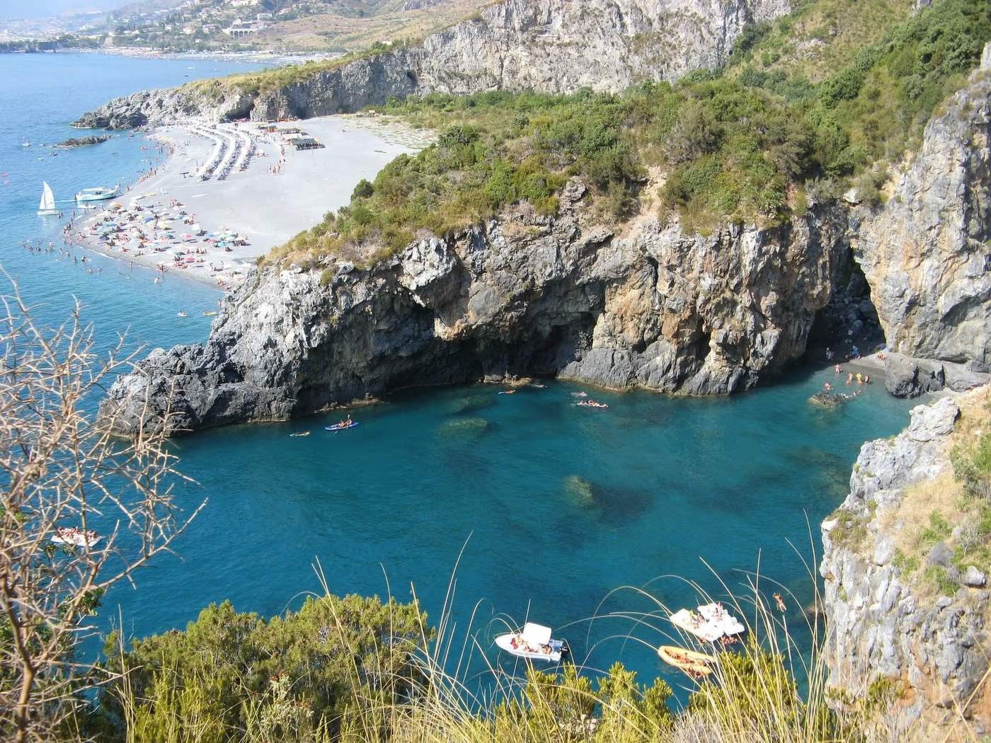 Vue aérienne d'une plage de la Calabre avec des falaises rocheuses et des eaux turquoise.