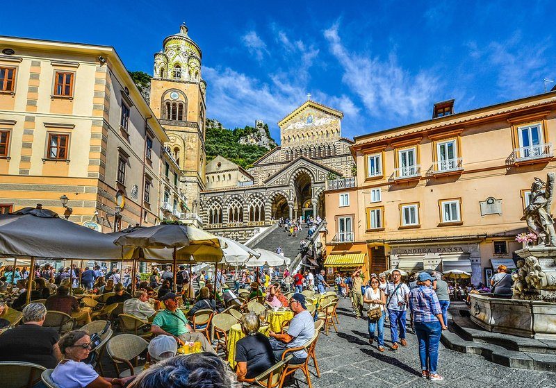 Scène animée à Amalfi avec des cafés en plein air et la cathédrale en arrière-plan.