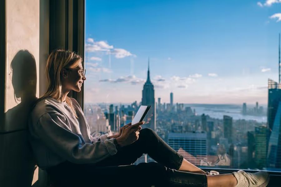 Femme souriante regardant New-Yorkpar une baie vitrée en tenant un téléphone dans ses mains connecté avec une esim