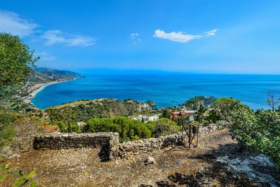 Vue panoramique de la côte de Sicile avec mer et collines verdoyantes.
