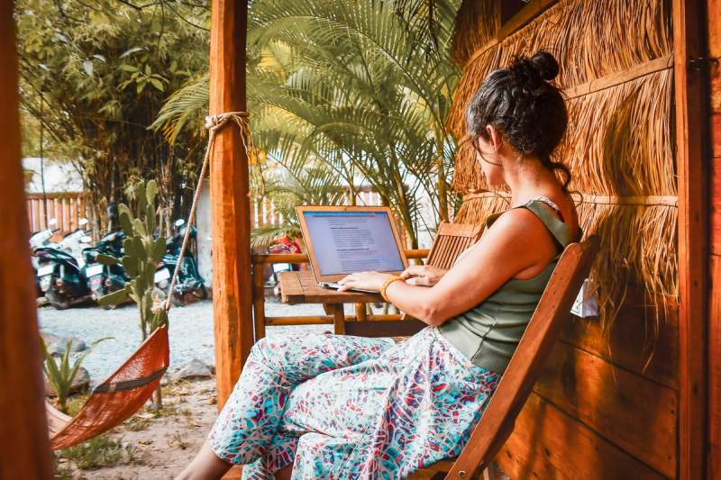 Femme travaillant sur un ordinateur portable dans un cadre tropical, illustrant le mode de vie des nomades numériques.