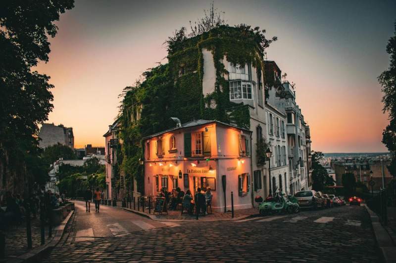 Vue crépusculaire de la Maison Rose dans le 18e arrondissement de Paris, avec ses façades couvertes de lierre et ses rues pavées pittoresques.