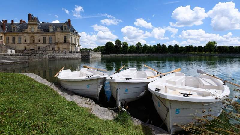 Trois bateaux à rames amarrés devant le château de Fontainebleau, France, sur un lac paisible.