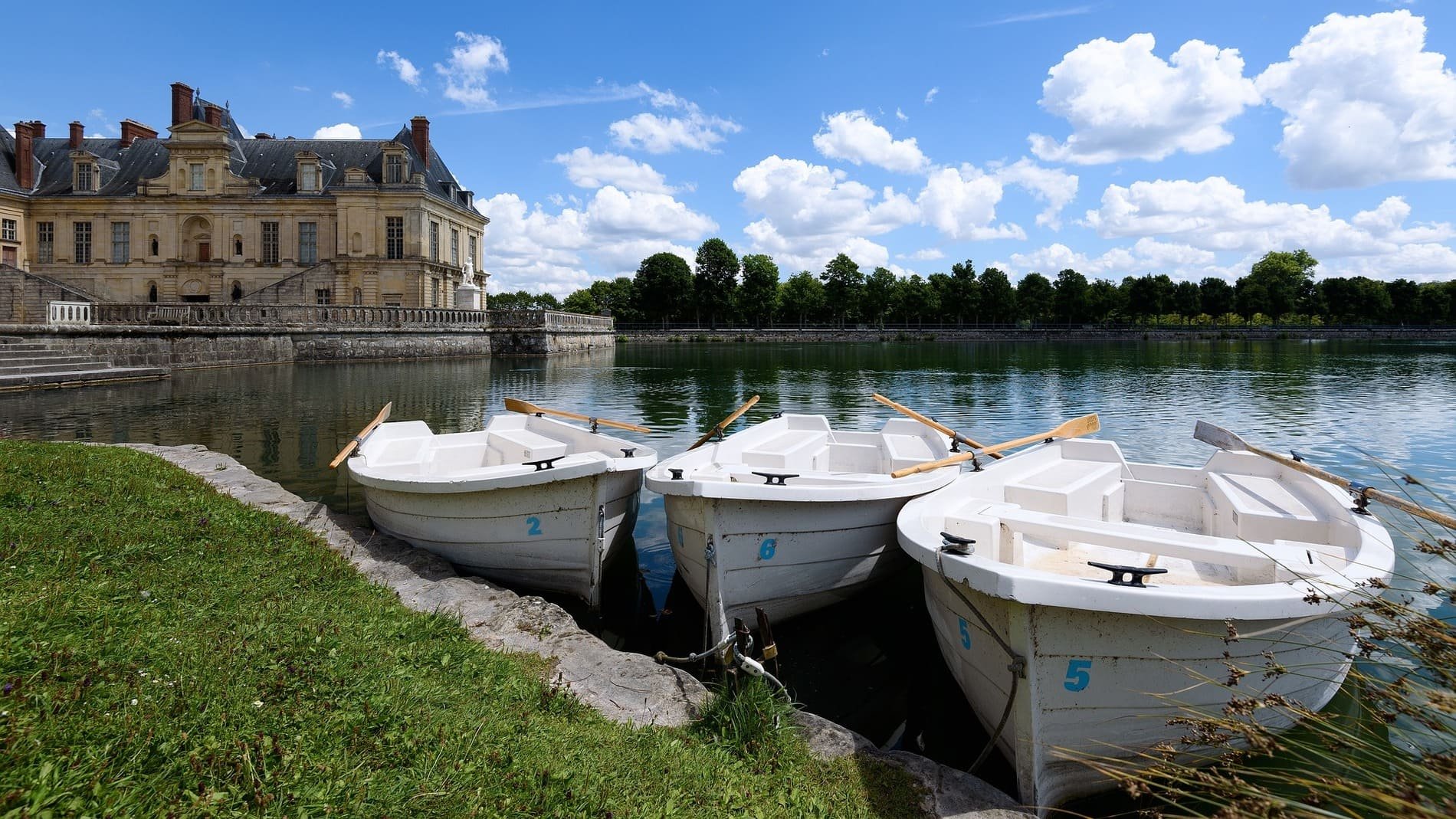 Trois bateaux à rames amarrés devant le château de Fontainebleau, France, sur un lac paisible.