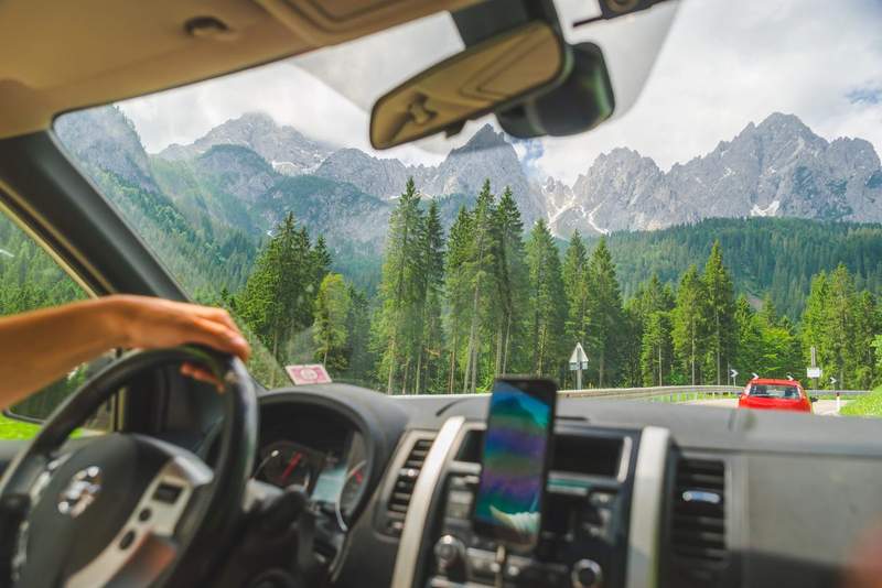 Vue depuis l'intérieur d'une voiture de location sur une route de montagne avec forêt de sapins et sommets rocheux
