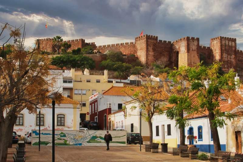 Vue du château de Silves surplombant les maisons traditionnelles de la ville, avec un ciel nuageux en arrière-plan, dans la région de l'Algarve au Portugal.