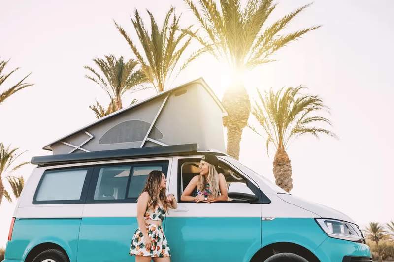 Van aménagé turquoise garé sous des palmiers, symbole de liberté et de voyage au soleil.