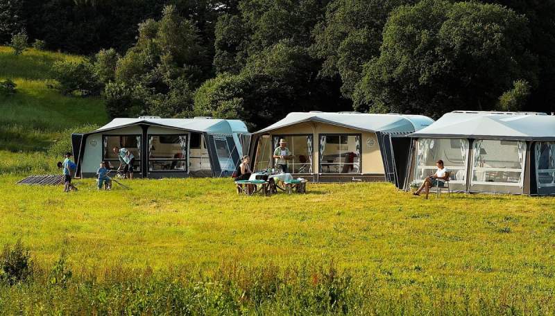 Vue sur des tentes de camping modernes installées dans un espace naturel verdoyant, avec des campeurs profitant de l’extérieur.