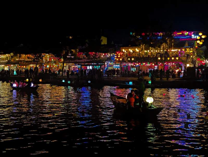 Vue nocturne de Hoi An Vietnam avec bateaux illuminés sur la rivière Thu Bon et façades décorées de lanternes colorées.