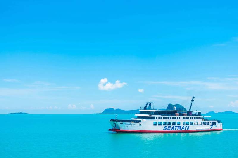 Un ferry de la compagnie Seatran naviguant dans une mer turquoise sous un ciel dégagé. En arrière-plan, des îles sont visibles, créant un paysage typique des voyages en Thaïlande.