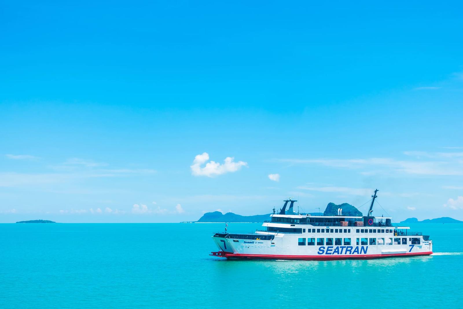 Un ferry de la compagnie Seatran naviguant dans une mer turquoise sous un ciel dégagé. En arrière-plan, des îles sont visibles, créant un paysage typique des voyages en Thaïlande.