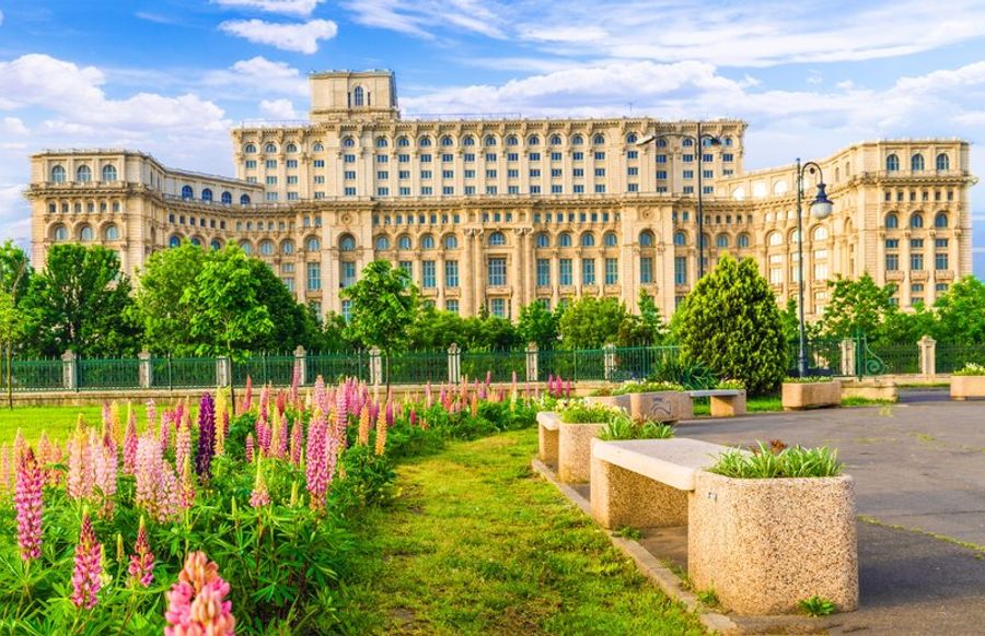 Façade massive du Palais du Parlement à Bucarest, entourée de jardins fleuris, illustrant l
