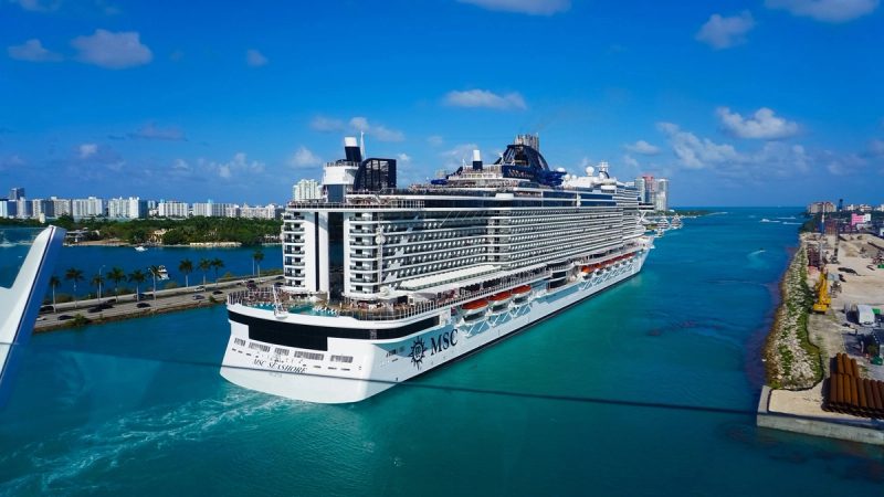 Navire de croisière MSC Seashore quittant le port de Miami par temps ensoleillé, avec les gratte-ciel en arrière-plan et les eaux turquoise.