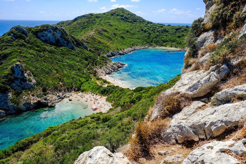 Vue aérienne des deux criques de Porto Timoni à Corfou, entourées de collines verdoyantes et de plages isolées aux eaux turquoise.