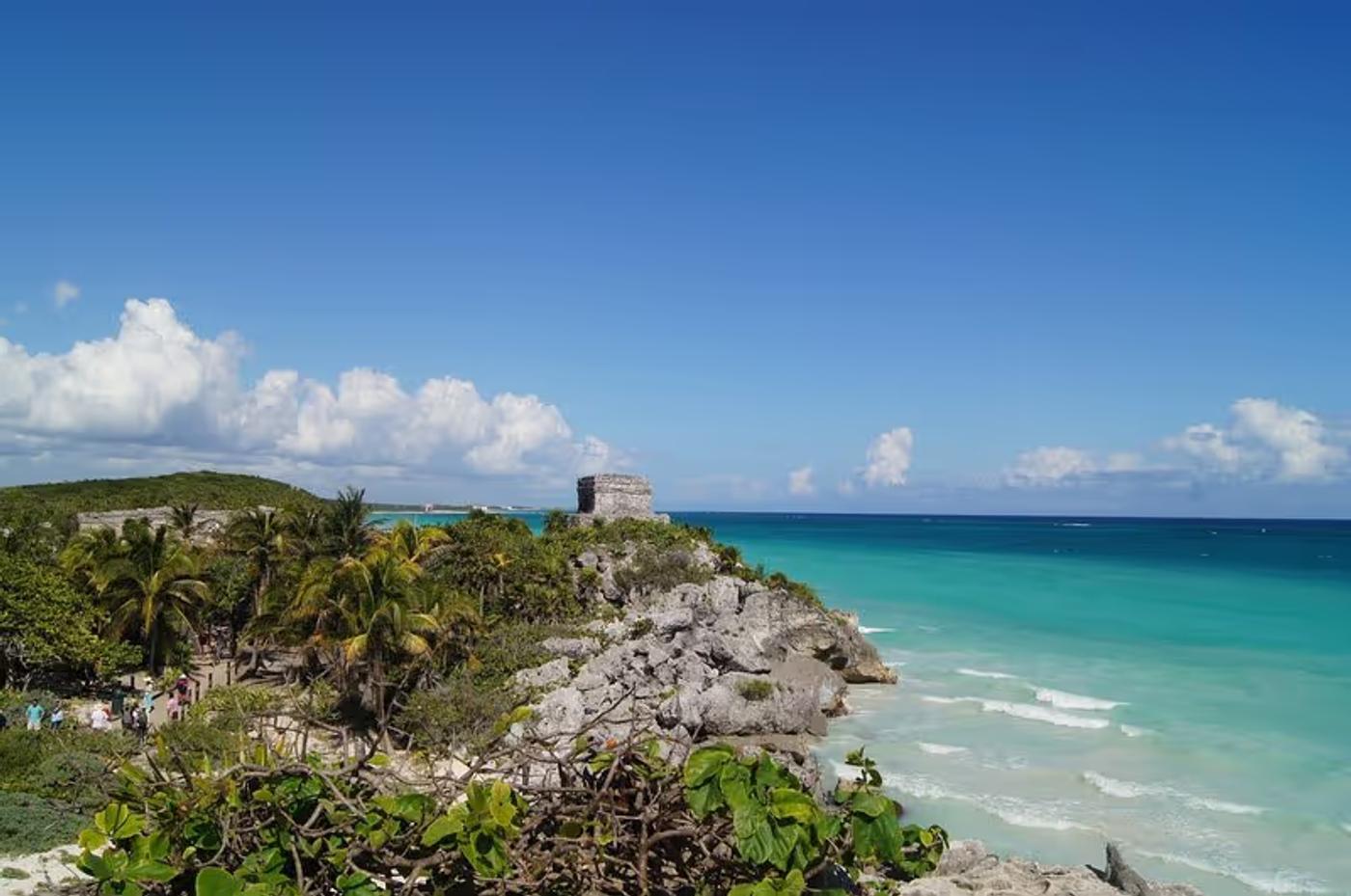 Vue panoramique des ruines mayas de Tulum, avec la mer turquoise à l’arrière-plan et un ciel bleu clair.