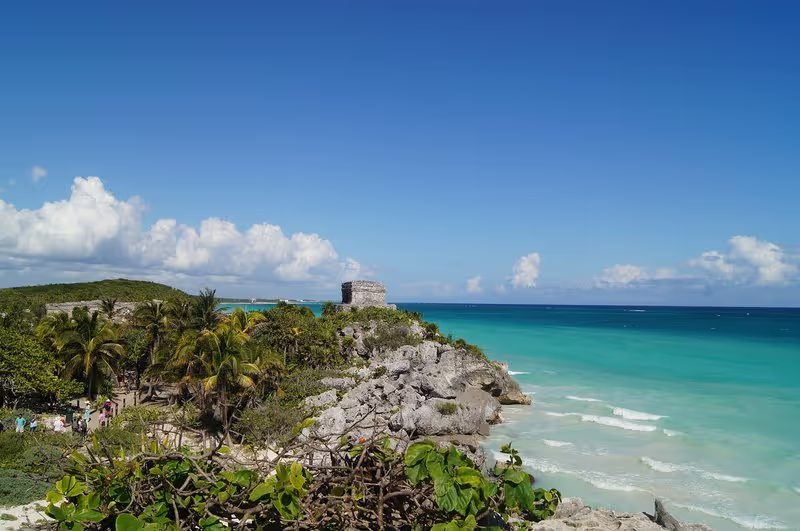 Vue panoramique des ruines mayas de Tulum, avec la mer turquoise à l’arrière-plan et un ciel bleu clair.