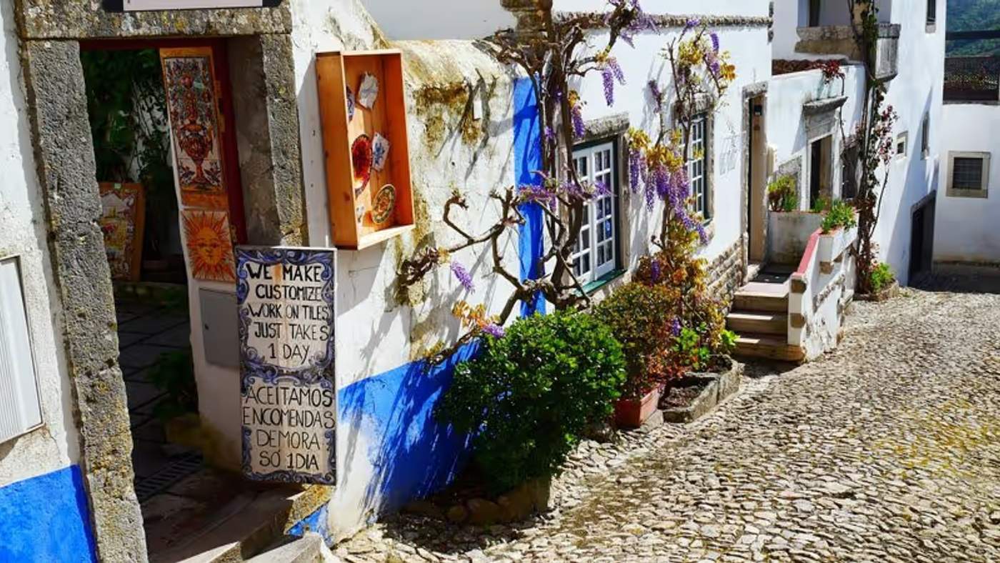 Rue pavée avec des maisons blanches et bleues, une boutique d'artisanat local à Obidos, Portugal.