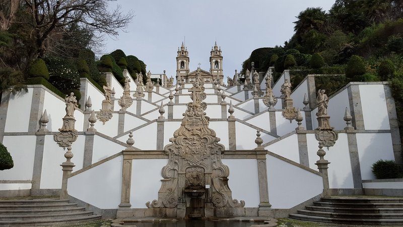 Escalier baroque du Sanctuaire du Bom Jesus do Monte à Braga, Portugal, avec des statues ornées et des haies parfaitement taillées. 