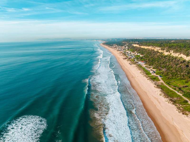 Vue aérienne de la longue plage de Costa da Caparica, Portugal, avec l'océan Atlantique et les vagues s'écrasant sur le rivage.