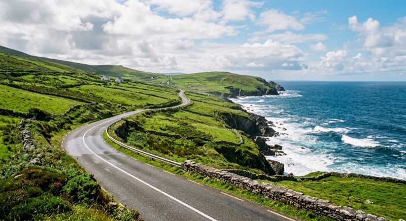 Route côtière sinueuse de la Wild Atlantic Way serpentant entre mer et collines vertes en Irlande.