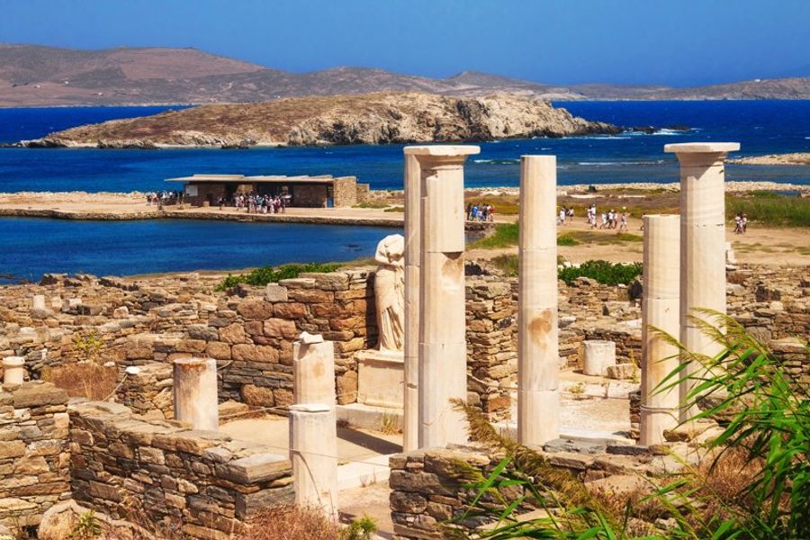 Ruines antiques de l’île de Délos avec des colonnes blanches et une vue sur la mer Égée.