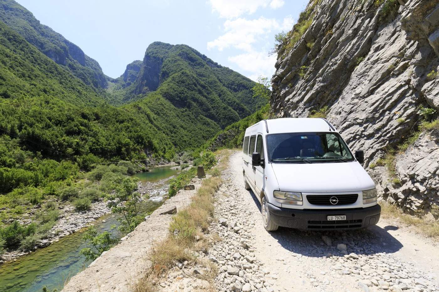 Minibus blanc sur une piste de gravier longeant une rivière dans les gorges de Valbona, Albanie