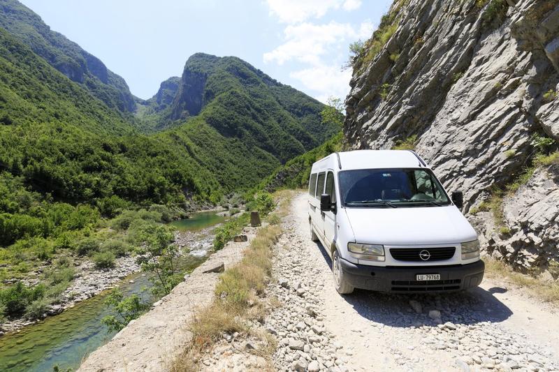 Minibus blanc sur une piste de gravier longeant une rivière dans les gorges de Valbona, Albanie