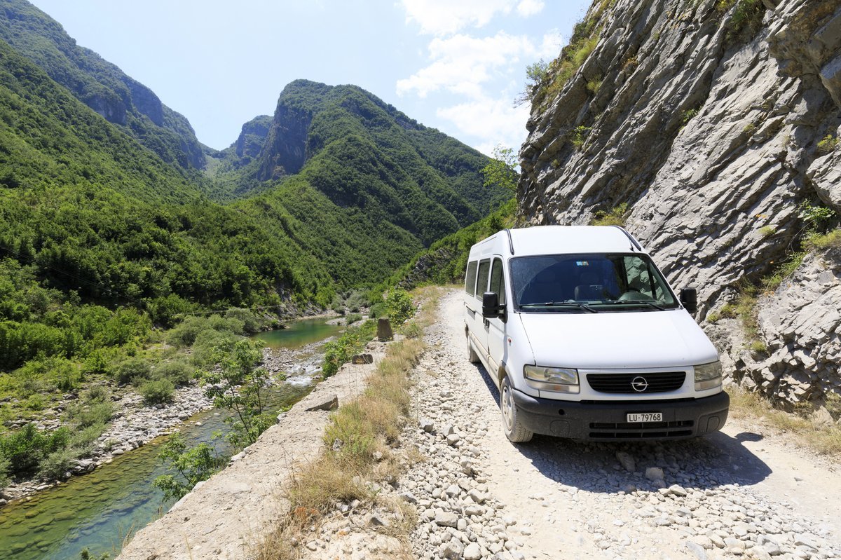 Minibus blanc sur une piste de gravier longeant une rivière dans les gorges de Valbona, Albanie