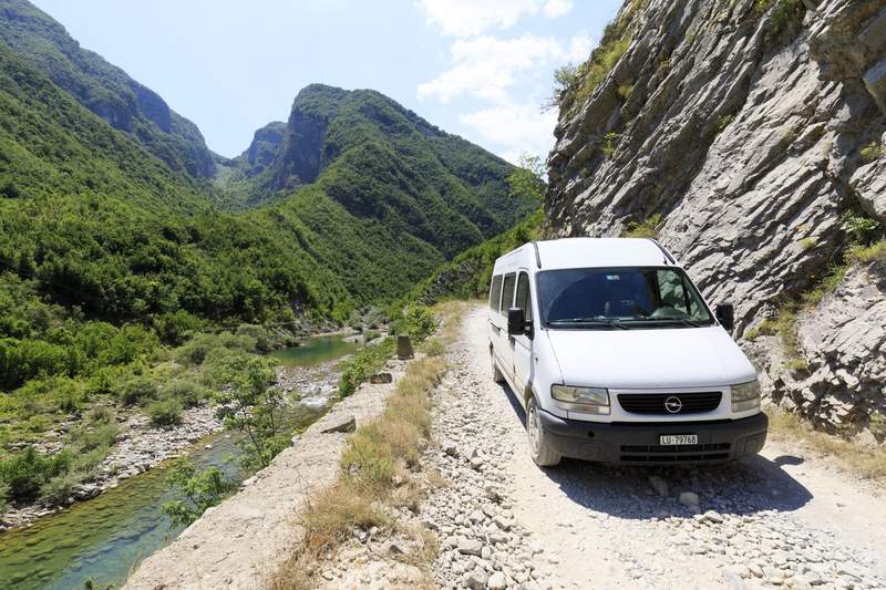 Minibus blanc sur une piste de gravier longeant une rivière dans les gorges de Valbona, Albanie