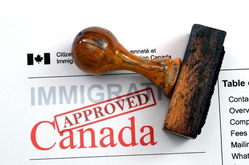 Tampon en bois marqué "Approved" sur un document officiel d'immigration canadienne.
