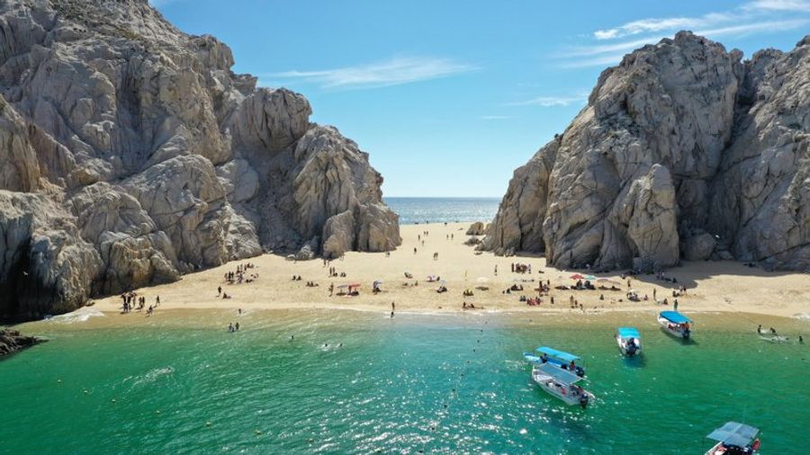 Vue de la plage de Cabo San Lucas, entourée de formations rocheuses impressionnantes avec des visiteurs et des bateaux.