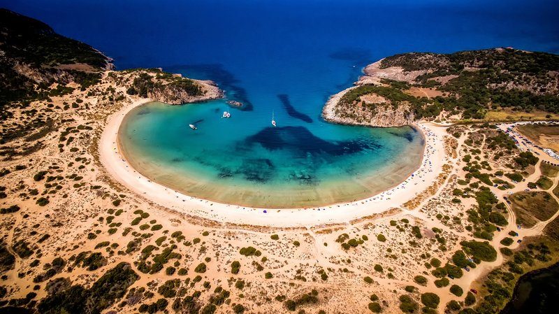 Vue aérienne de la plage de Voidokilia, célèbre pour sa forme en oméga, avec du sable blanc et des eaux turquoises.