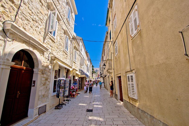 Une rue pittoresque bordée de bâtiments en pierre dans la ville de Pag, en Croatie, avec des boutiques et des passants.