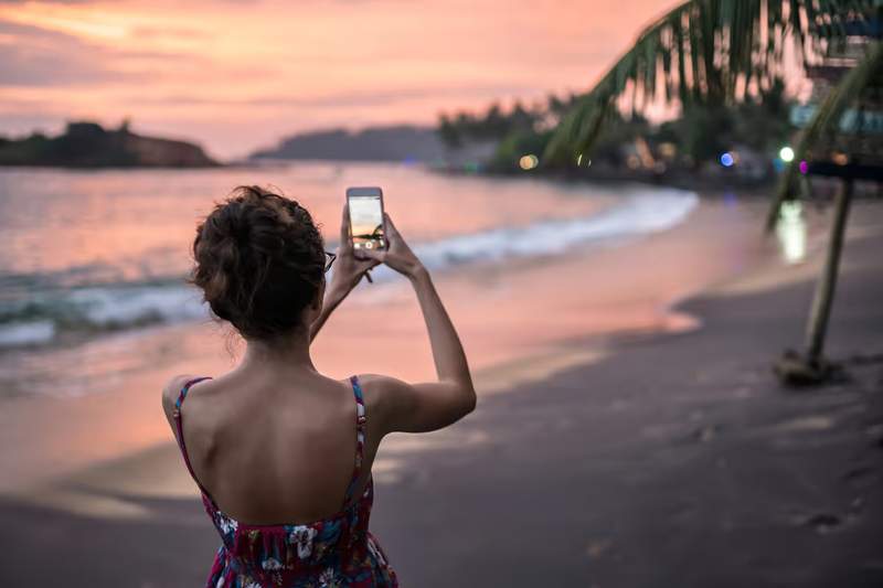 Voyageuse photographiant le coucher de soleil sur une plage thaïlandaise avec son smartphone connecté en eSIM