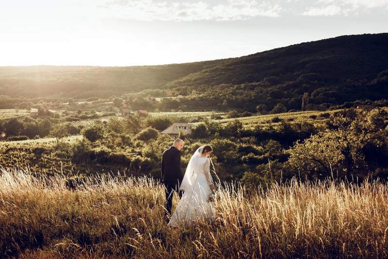 Couple de mariés marchant dans un champ au coucher du soleil avec vue sur les collines et la vallée.