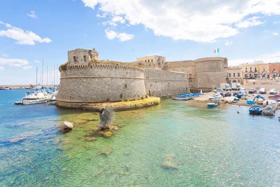 Vue du château de Gallipoli entouré d’eau cristalline et de bateaux de pêche.