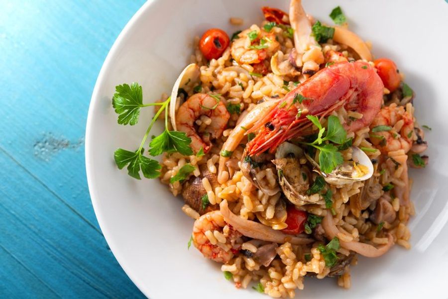Assiette appétissante de risotto aux fruits de mer, garnie de crevettes, palourdes et persil frais.