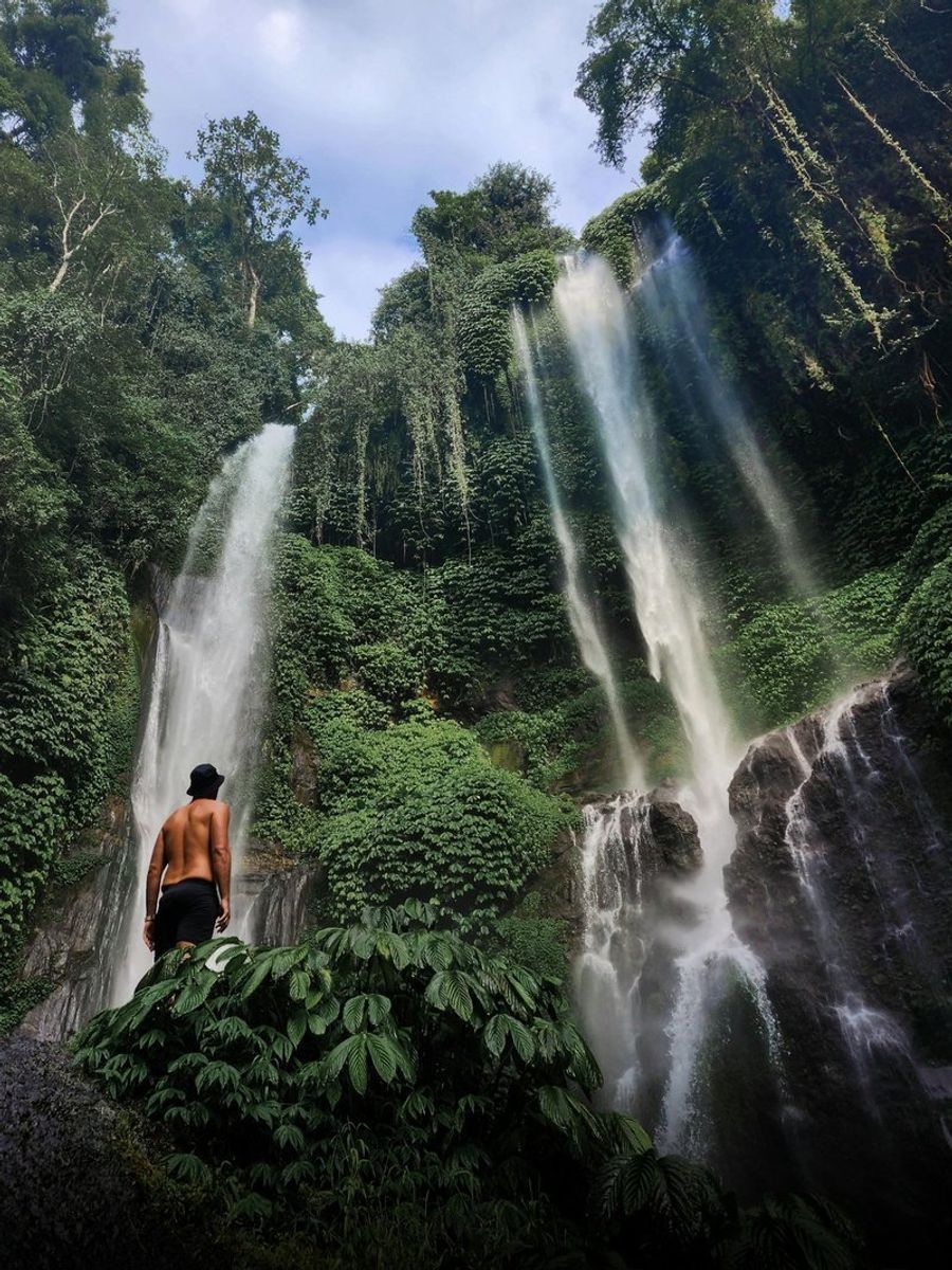 Cascade de Sekumpul avec une végétation luxuriante autour et un homme contemplant la chute d
