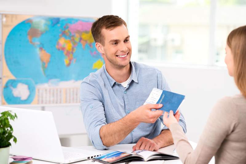 Agent de voyage remettant des billets à une cliente dans une agence avec une carte du monde en arrière-plan