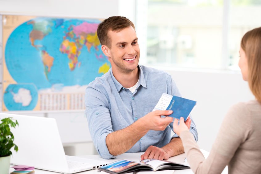 Agent de voyage remettant des billets à une cliente dans une agence avec une carte du monde en arrière-plan